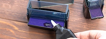 picture of a hand holding ink bottle, adding ink to self-inking stamp pad 